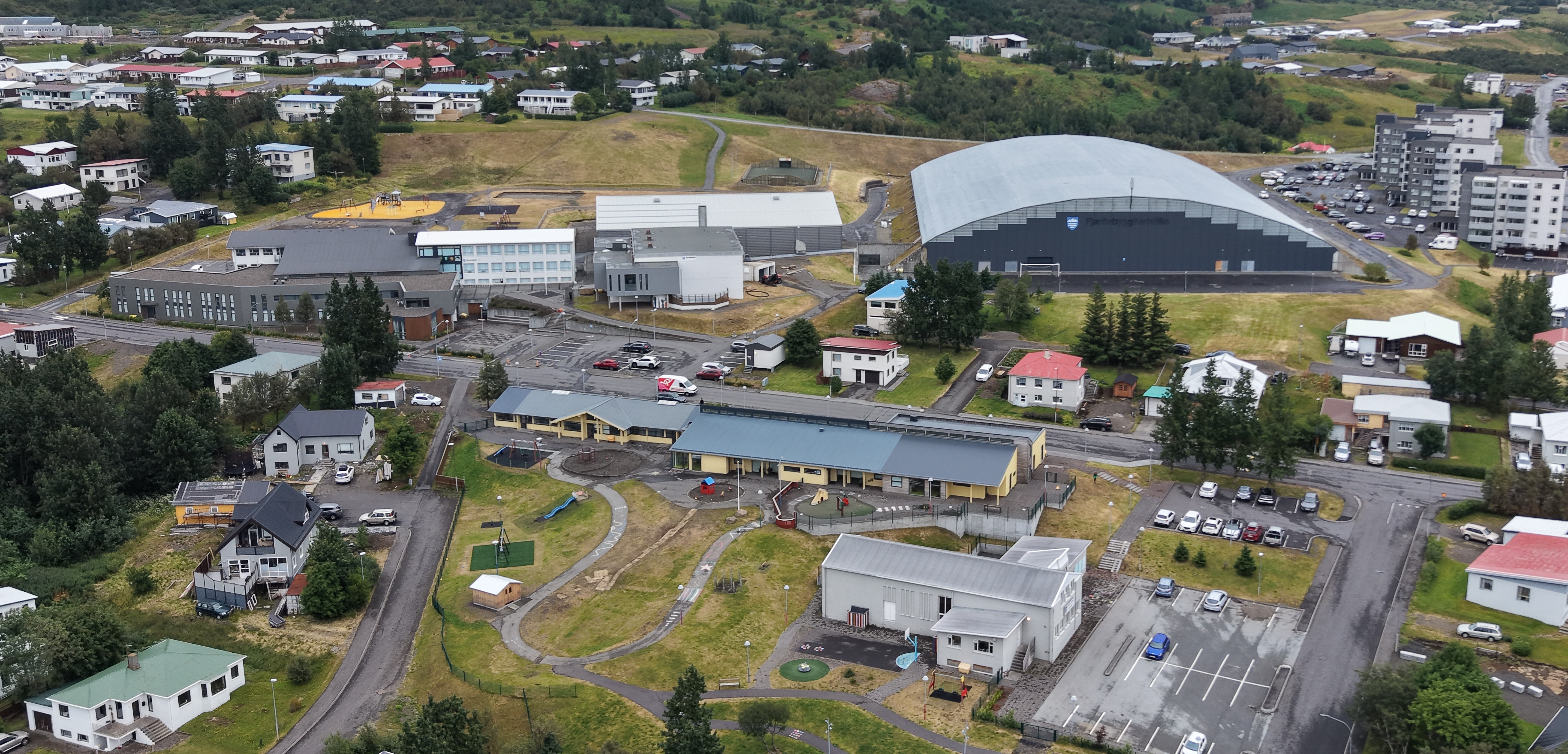 Loftmynd yfir Fjarðabyggðarhöllina og nærliggjandi byggingar á Reyðarfirði, þar á meðal skóla, íþróttahús og leikskóla.