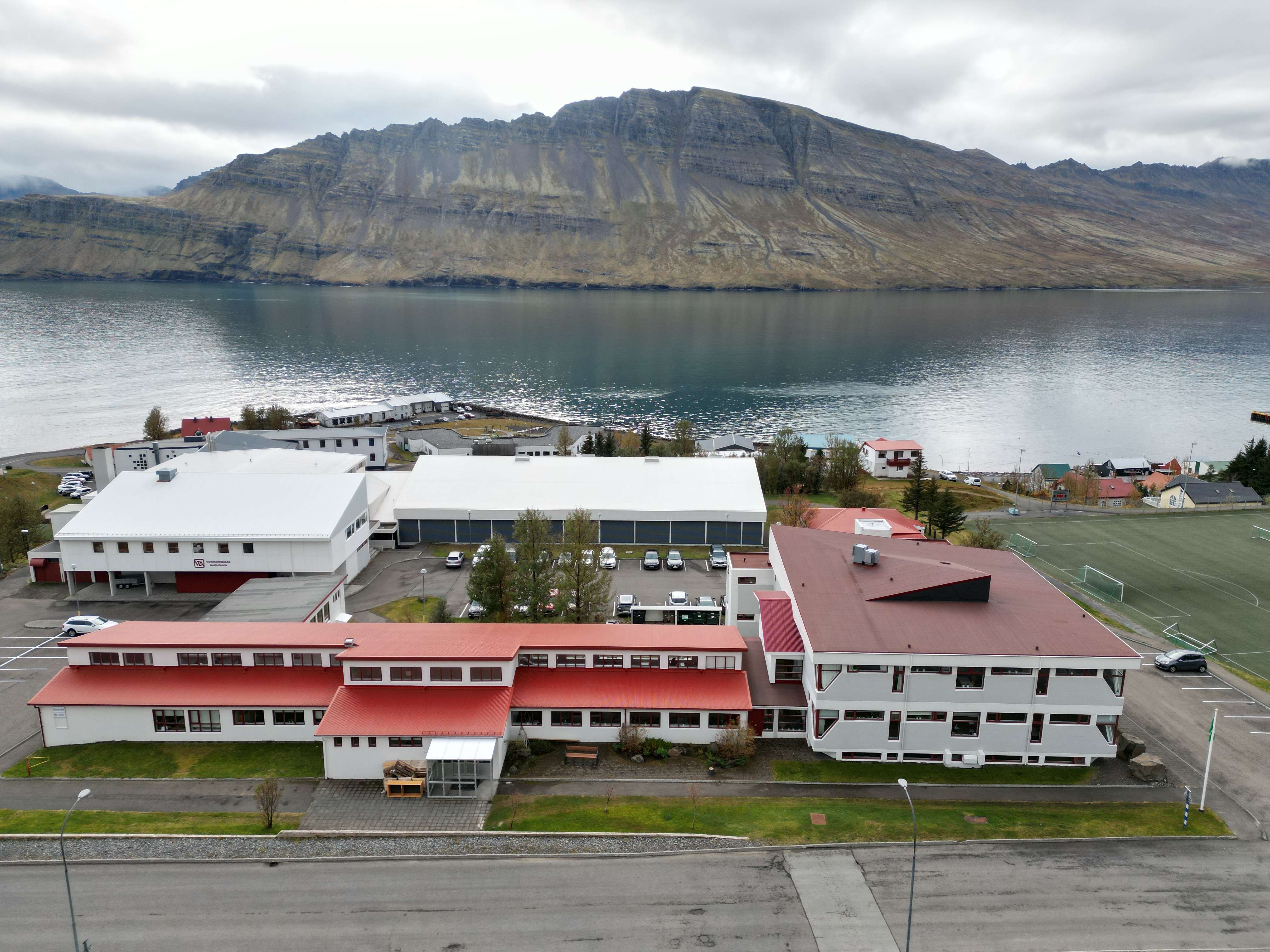 Loftmynd af húsnæði Verkmenntaskóla Austurlands og íþróttamiðstöð Fjarðabyggðar í Neskaupstað, með Norðfjörð og fjöllin handan fjarðar í bakgrunni.