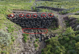Grjótstífla í grónum farvegi. Rauðar merkingar sýna grjót efst á stíflunni og neðan hennar sem á að fjarlægja.