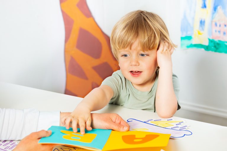 Kindergarten development lesson - little blond boy point to letters on the page in the book